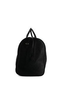 Zaino in pelle nera con superficie texturizzata, forma arrotondata, doppi manici superiori e chiusura a zip frontale. Design minimalista senza decorazioni.