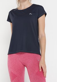 Námorně modré sportovní tričko s krátkým rukávem a kulatým výstřihem, vyrobené z prodyšného materiálu, spárované s růžovými texturovanými legínami s vzorem.