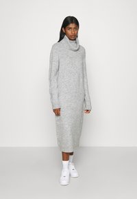 Ανοιχτό γκρι πλεκτό φόρεμα με ψηλό λαιμό, μακριά μανίκια και ραμμένα μανσέτα, με ευθεία σιλουέτα που πέφτει κάτω από το γόνατο.