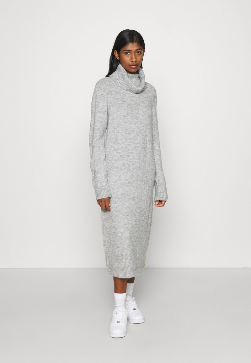 Ανοιχτό γκρι πλεκτό φόρεμα με ψηλό λαιμό, μακριά μανίκια και ραμμένα μανσέτα, με ευθεία σιλουέτα που πέφτει κάτω από το γόνατο.