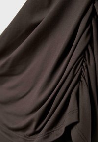 Donkerbruine stof met geplooide plooien en een gladde textuur, die zachte plooien en zichtbare stiksels langs de rand creëert.