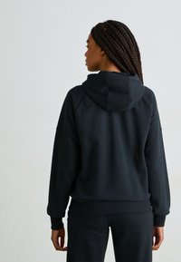 Sweatshirt preto feito de um tecido macio, apresentando um corte descontraído, mangas raglan e capuz. Os punhos e a bainha canelados proporcionam estrutura.