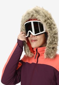 Giacca da sci con cappuccio foderato in pelliccia sintetica; presenta pannelli di un vivace corallo e un profondo viola; dotata di occhiali bianchi eleganti.