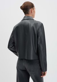 Schwarze Kunstleder-Cropped-Jacke mit klassischem Kragen und glatter Textur, kombiniert mit hochgeschnittenen grauen Jeans, von hinten betrachtet.