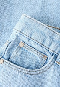 Svijetloplava traper tkanina s malim prednjim džepom i dva metalna gumba. Šavovi su u kontrastnoj smeđoj boji.