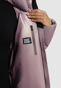 Polstret pink jakke med quiltet tekstur og sorte accenter. Funktioner en frontlynlås og et logo patch på brystområdet.