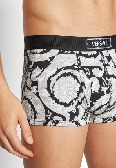 Boxeri negri cu un model floral alb și un model spiralat, confecționați dintr-un material elastic, cu un talie elastică neagră.