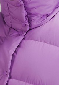 Doudoune violette avec un col montant, des fermetures à boutons-pression et une texture matelassée pour plus de chaleur et de confort.