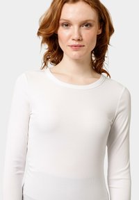 Witte longsleeve top van ribstof. Heeft een ronde halslijn en een getailleerde pasvorm, met een zachte textuur en minimale details.