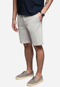 Helle graue Shorts aus einem weichen Material, mit zwei Seitentaschen und geradem Schnitt. Kombiniert mit hellgrauen Slippern.