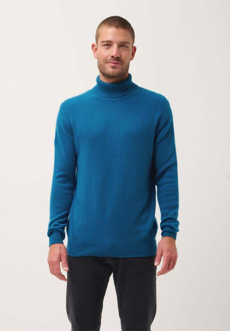 Maglione a collo alto turchese realizzato in un morbido tessuto a maglia; presenta maniche lunghe e un orlo e polsini a coste. Indossato con jeans scuri.