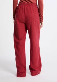 Czerwone spodnie w kratkę z elastycznym paskiem w talii, luźnym kroju i zwężanymi mankietami. Wykonane z miękkiego materiału o subtelnej teksturze.