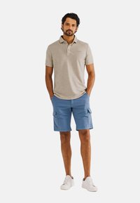 Grijze polo met een kraag en knopen, gecombineerd met blauwe cargo shorts met zijzakken. Witte sneakers maken de outfit compleet.