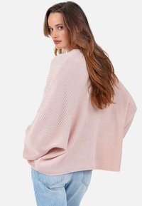 Pull en maille côtelée rose clair avec une coupe ample et décontractée et des épaules tombantes, associé à un jean bleu clair.