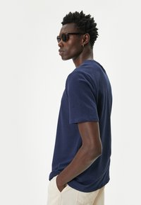 Camiseta de manga corta navy en tejido texturizado, con cuello redondo y corte relajado. El modelo lleva gafas de sol oscuras.
