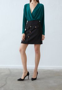 Tyrkysový dlouhý rukávový top s hlubokým výstřihem do V, v kombinaci s černou upnutou sukní s předními knoflíky a kapsami s klopou. Nosí se s černými lodičkami.