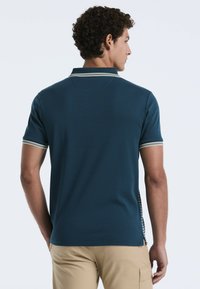 Polo T-shirt in donker teal met korte mouwen, featuring gestreepte accenten op de kraag en mouwen, en een gestructureerd achterpaneel ontwerp.