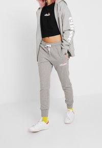 Ljusgrå sweatshirt och sweatpants-set med en croppad svart topp. Vita logotypdetaljer och gula strumpor tillsammans med vita sneakers.