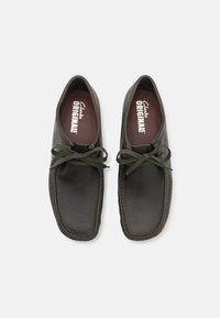 Par av mörkbruna läder Clarks Originals skor med rundade tår, sydda detaljer och knutna gröna snören, sedd uppifrån.