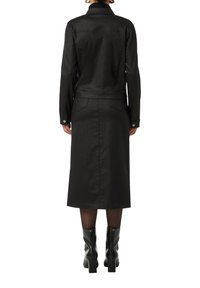 Czarna dżinsowa kurtka ma kołnierzyk i dopasowany krój, w połączeniu z pasującą czarną spódnicą. Modelka nosi błyszczące kozaki do kolan.