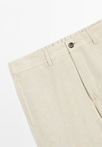 Beige linen trousers with belt loops, side pockets, a button closure, and a visible waistband, shown against a white background.