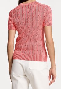 Pull en tricot à manches courtes, rose corail, avec un motif en câble ; col et ourlet côtelés ; texture lisse ; silhouette ajustée.