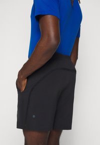 Schwarze Sportshorts mit glatter Textur, seitlichen Taschen und einem dezenten Logo. Der Bund ist elastisch für zusätzlichen Komfort.