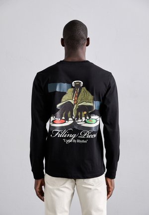 Schwarzes Langarm-T-Shirt mit einem bunten Grafikmotiv eines DJs mit Kopfhörern, darunter die Texte "Filling Pieces" und "United By Rhythm".