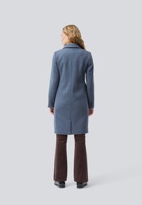 Blue wool coat with a tailored fit, long sleeves, and notched collar. Paired with brown corduroy pants and black footwear.