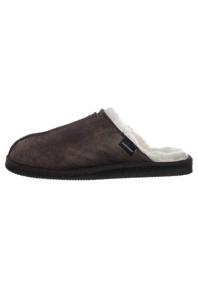 Tummanruskea liukupohjainen tossu, jossa on pehmeä valkoinen fleece-vuori ja musta pohja. Sivulapussa lukee "Shepherd."