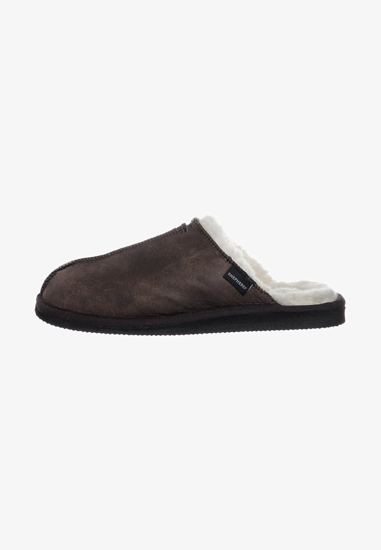 Tummanruskea liukupohjainen tossu, jossa on pehmeä valkoinen fleece-vuori ja musta pohja. Sivulapussa lukee "Shepherd."