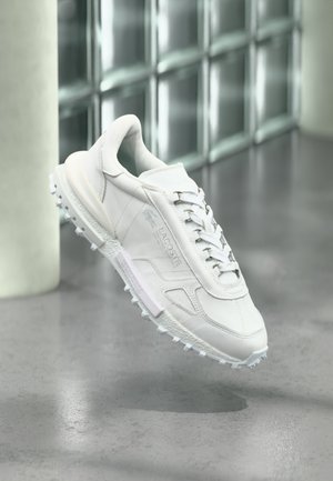 White athletic shoe with perforated leather, textured accents, and rubber traction outsole. Features silver laces and a logo on the side.