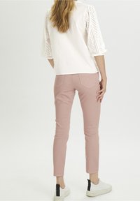 Top bianco con maniche a lavoro a maglia aperto, abbinato a pantaloni fitted rosa chiaro e sneakers bianche con un accento nero sul retro.