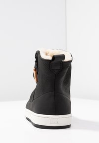 Botín negro de cuero con un suave forro de forro polar color crema, lengüeta trasera y suela de goma blanca con la marca "HUB".