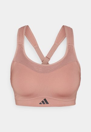 Lichtroze sportbeha met meshpanelen, kruisbandjes en een opvallend zwart logo-accent aan de onderkant. Soepele textuur.