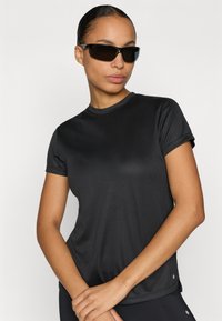 Schwarzes, kurzärmeliges Sport-T-Shirt aus glattem Stoff mit Rundhalsausschnitt und dezenten seitlichen Schlitzen, kombiniert mit einer schwarzen Sonnenbrille.