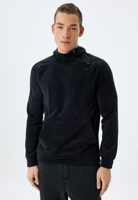 Svart fleece-pullover med hög krage, framficka och dragkedja. Mjuk textur och figurnära design, i kombination med matchande mörka sweatpants.