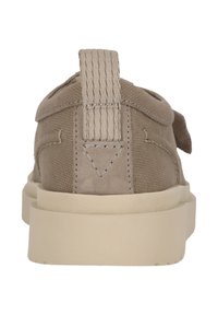 Beige lærredssneaker med struktureret overdel, flad gummisål og syede detaljer. Har en træksløjfe ved hælen og et diskret design.