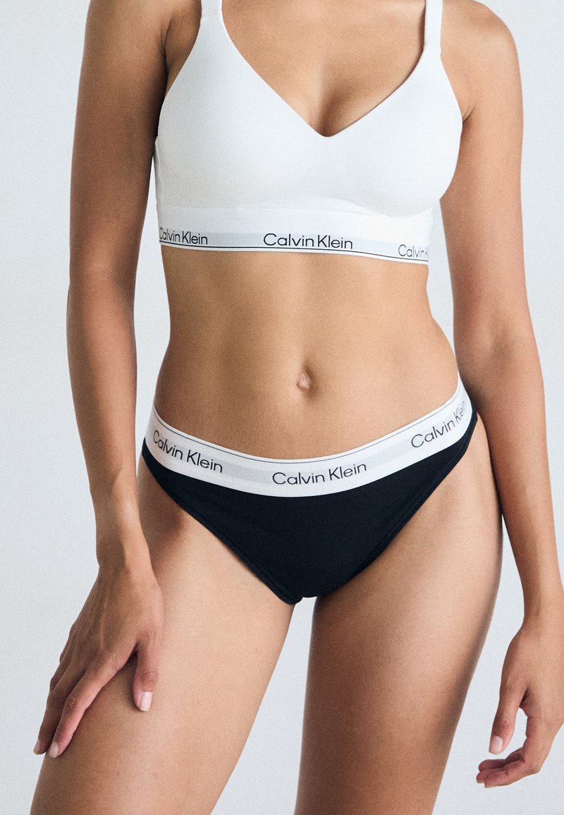 Crni pamučni bikini s bijelim pojasom na kojem je istaknut "Calvin Klein" logo; u paru s bijelim pamučnim braletom sličnog brendiranja.