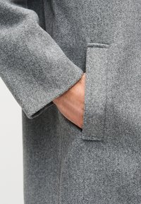 Γκρι μάλλινο παλτό με υφή, διαθέτει πλευρική τσέπη και έντονη λεπτομέρεια στον μανσέτα. Το υλι κό φαίνεται μαλακό και ζεστό.