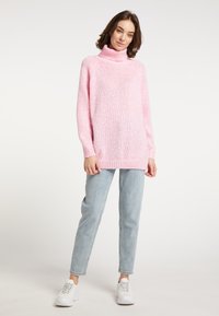Suéter de punto rosa claro con cuello alto, mangas largas y un corte relajado, combinado con jeans azul claro y zapatillas blancas.