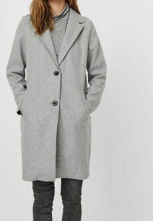 Kobieta nosząca jasnoszary, wełniany płaszcz do kolan z dwoma czarnymi guzikami, kieszeniami bocznymi oraz szary golf pod spodem.