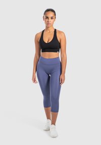 Top sportivo nero a coste con spalline larghe, abbinato a leggings blu navy a vita alta e scarpe da ginnastica bianche. Design semplice e aderente.