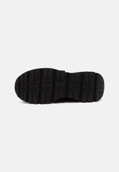 Semelle de chaussure noire avec des crampons profonds et des motifs géométriques conçus pour l'adhérence et la durabilité, présentée sur fond blanc.