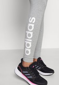 Grå leggings med stort vitt "adidas"-logotyp längs sidan, kombinerat med svarta träningsskor med rosa detaljer och en texturerad nätövre.