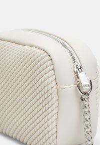 Borsa a tracolla bianca intrecciata con superficie testurizzata, chiusura con zip argentata e un accent metallico a catena attaccato al lato.