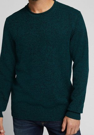 Mand iført mørk teal crewneck langærmet sweater med ribstrikkede manchetter og kant, kombineret med mørkeblå jeans.