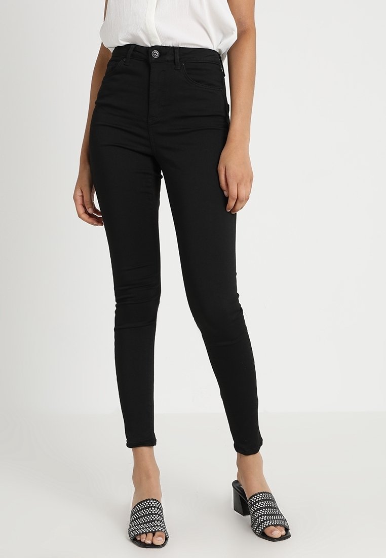 Jean noir taille haute et coupe slim, porté avec un haut blanc et des sandales à talons ouvertes noires avec un motif tissé.