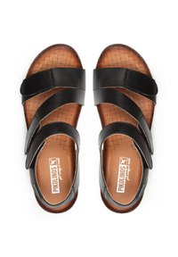 Sandalias de cuero negro con dos correas anchas, plantillas marrón texturizadas y forma contorneada. Etiqueta visible en la plantilla.