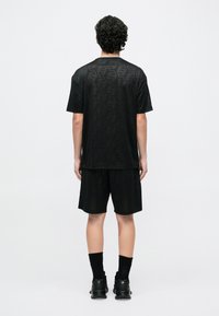 Melnas sporta apģērbs, kas sastāv no īss piedurkņu T-krekla ar apaļu kaklu un atbilstošiem šortiem, kuros ir smalks sešstūra raksts un elpojošs materiāls.